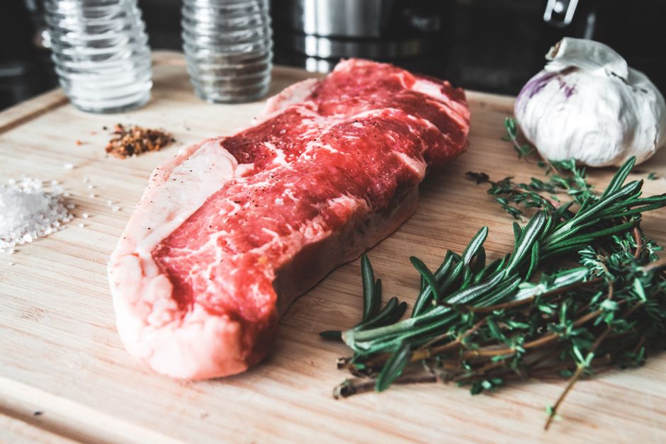 Close-up of raw striploin steak on a wooden cutting board with garlic, rosemary, and seasoning.